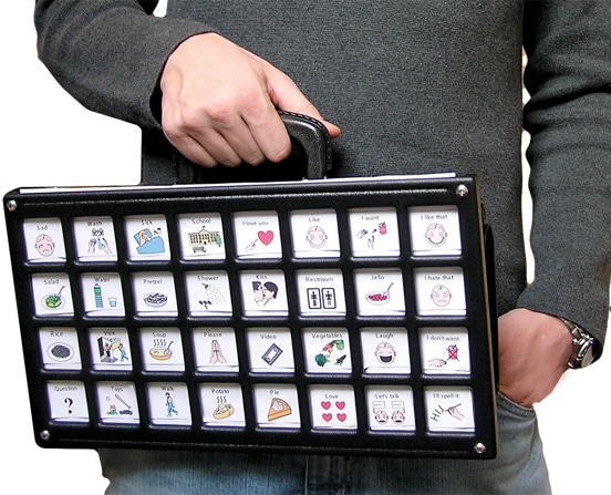 A rectangular AAC device with a grid of message buttons under a clear overlay frame, adjustable legs, and a carrying handle.