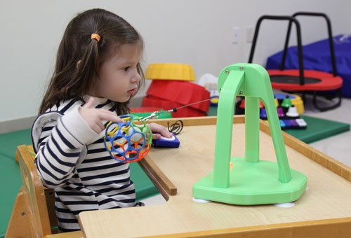 A colorful ball tethered to a base unit, shown beside a child reaching to pull it.