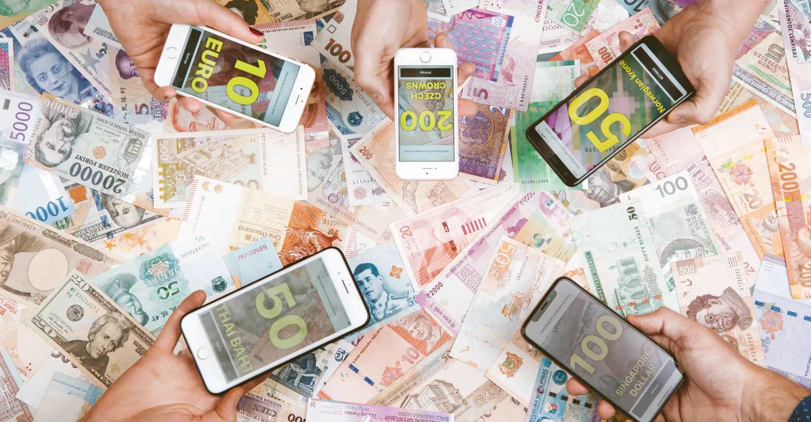 Five hands holding phones over a spread of banknotes from around the world, each phone naming a different currency in large yellow text.
