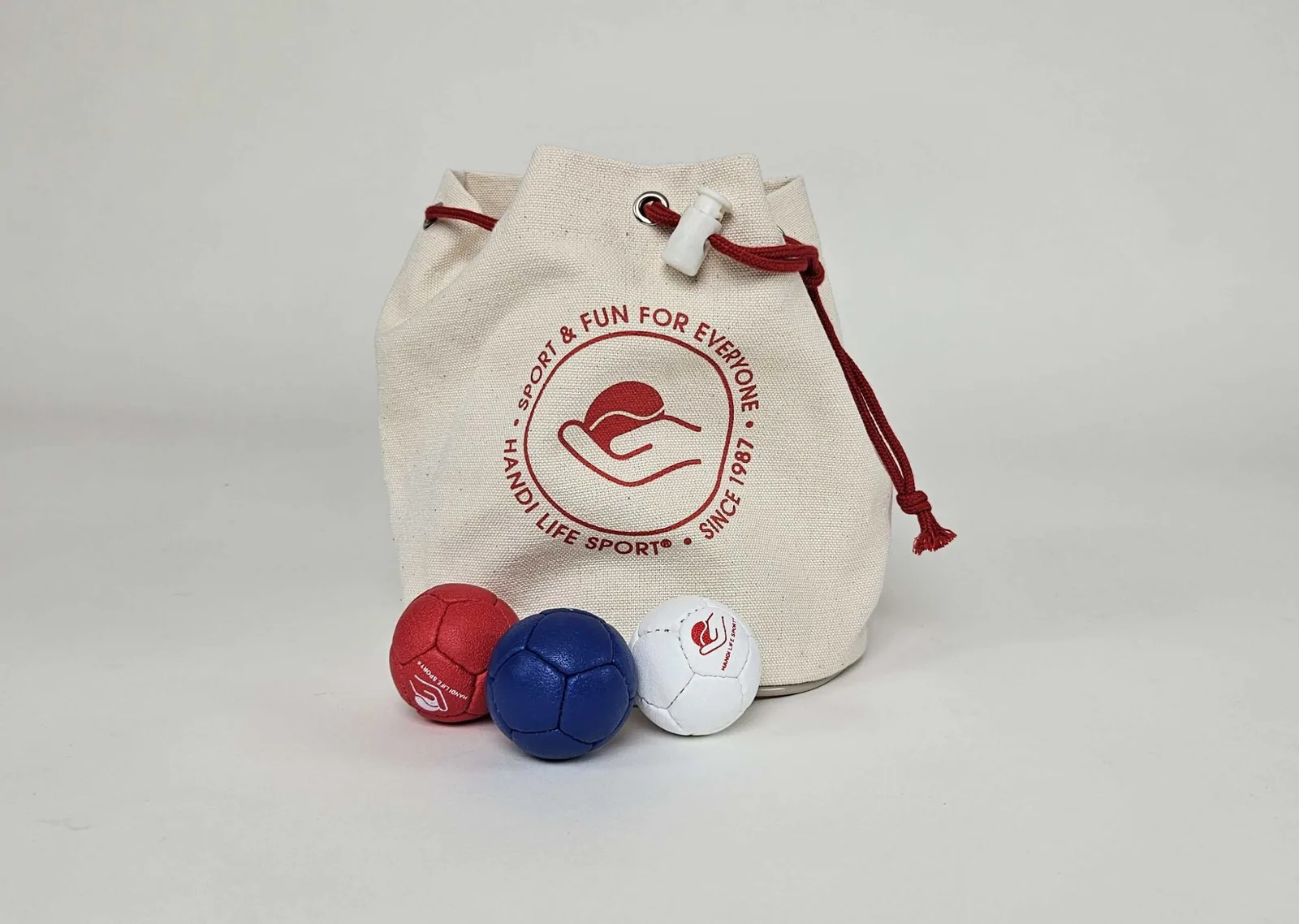 A natural canvas drawstring bag with three small boccia balls in red, blue and white.