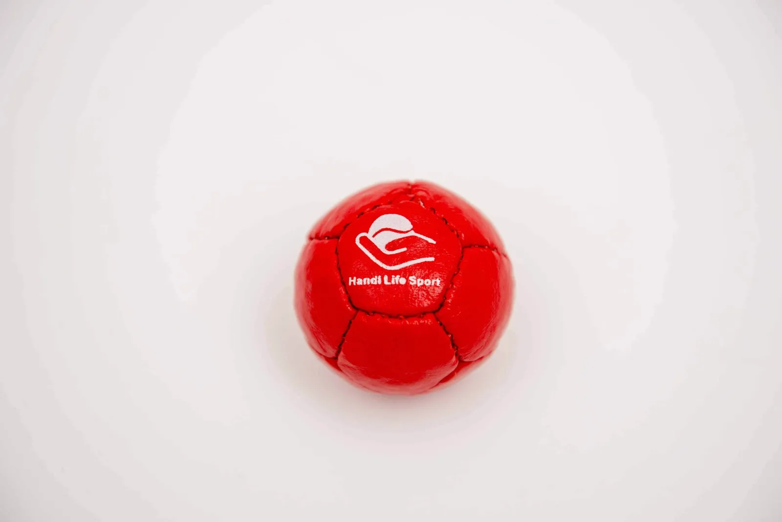 A small red soft leather petanque target ball with the Handi Life Sport logo.