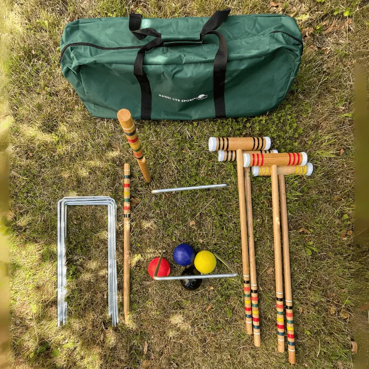 A lawn croquet set on grass: a green bag, metal hoops, wooden mallets and coloured balls.
