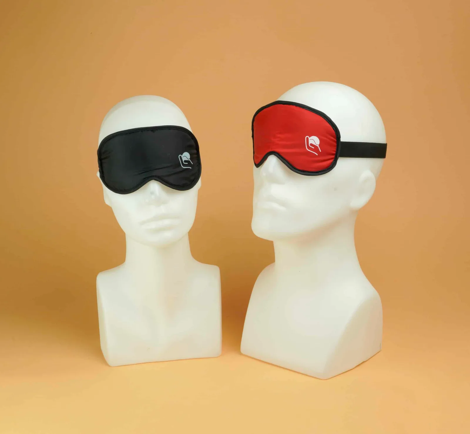 Two display heads wearing soft fabric eye masks, one black and one red.
