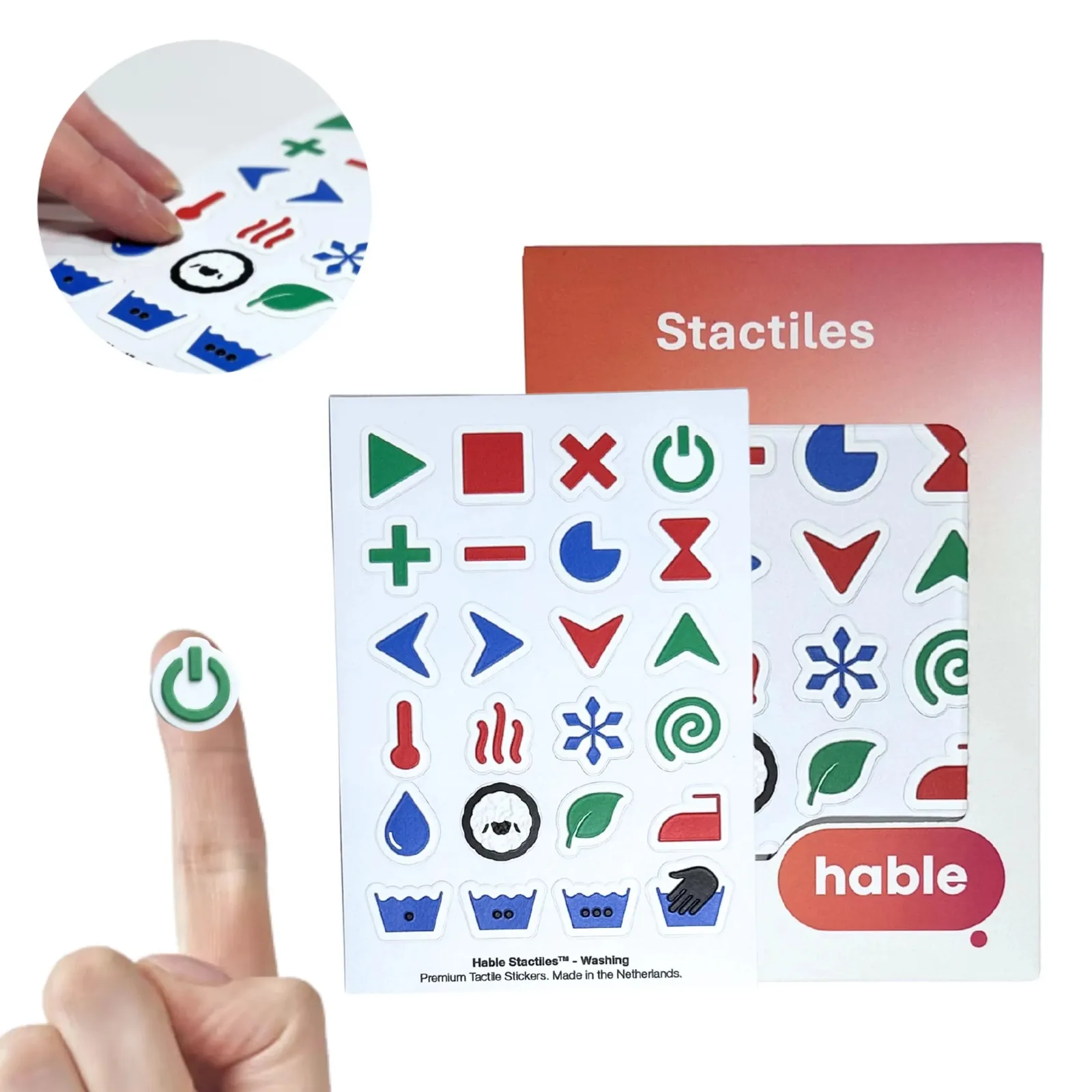 The Hable Stactiles Washing set: a white sticker sheet covered in raised laundry icons such as a thermometer, heat waves, a snowflake, a woolly sheep, a leaf, an iron and wash-tub symbols, shown in front of its orange Hable box. A fingertip rests on a green power-button sticker, and an inset close-up shows fingers feeling the raised stickers.