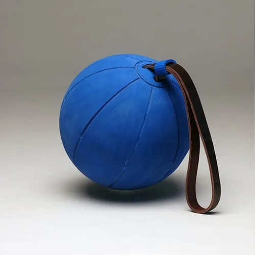 A blue rubber ball with a long brown leather loop sewn into its top, hanging down to the right.