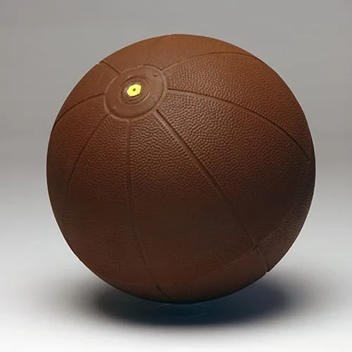 A brown medicine ball with a heavily pebbled rubber surface, segmented panels and a yellow valve at the top.